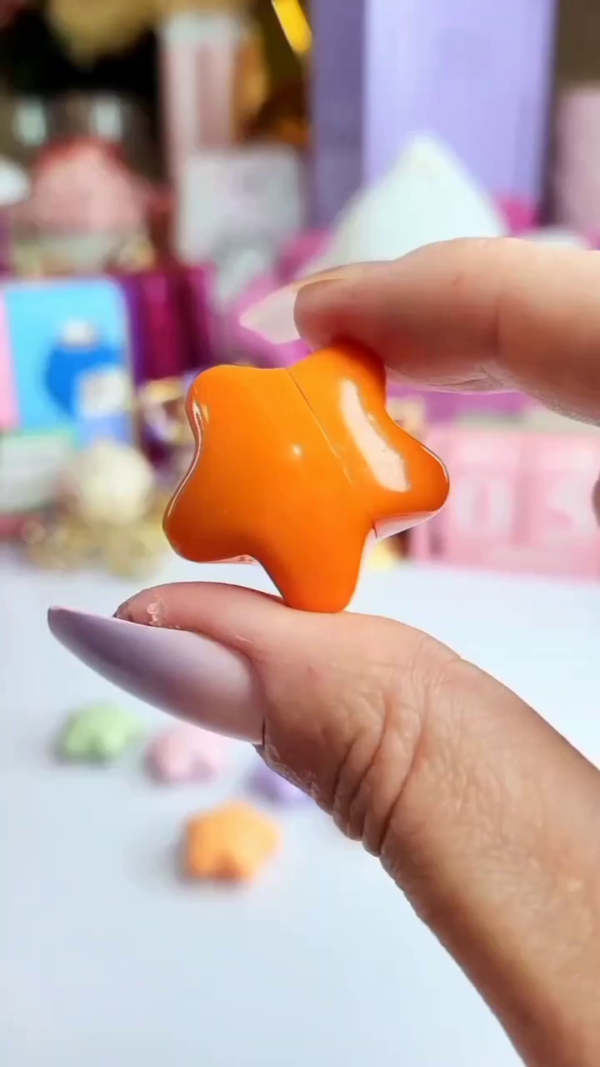 A vibrant orange star-shaped lip balm is being swatched on the hand, leaving a soft, pinkish tint. - Image 3